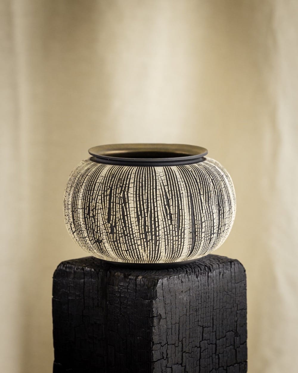 Round ceramic bowl with black and white crackle glaze on a charred wood block