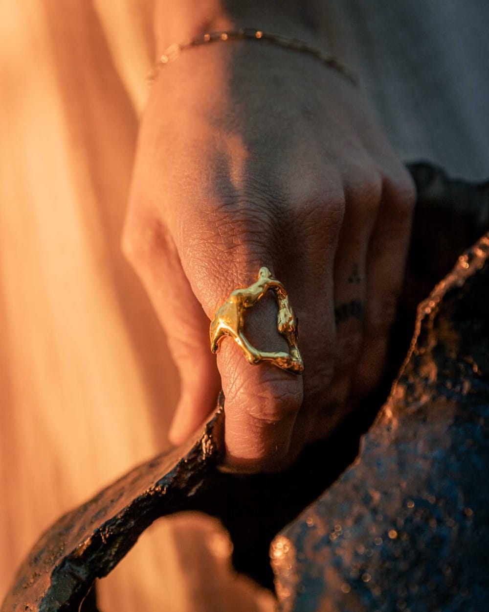 Hand with a gold ring resting on dark glazed ceramic in warm light