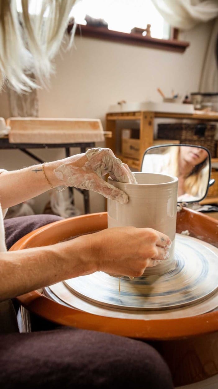 Clay-covered hands throwing a pot on the wheel