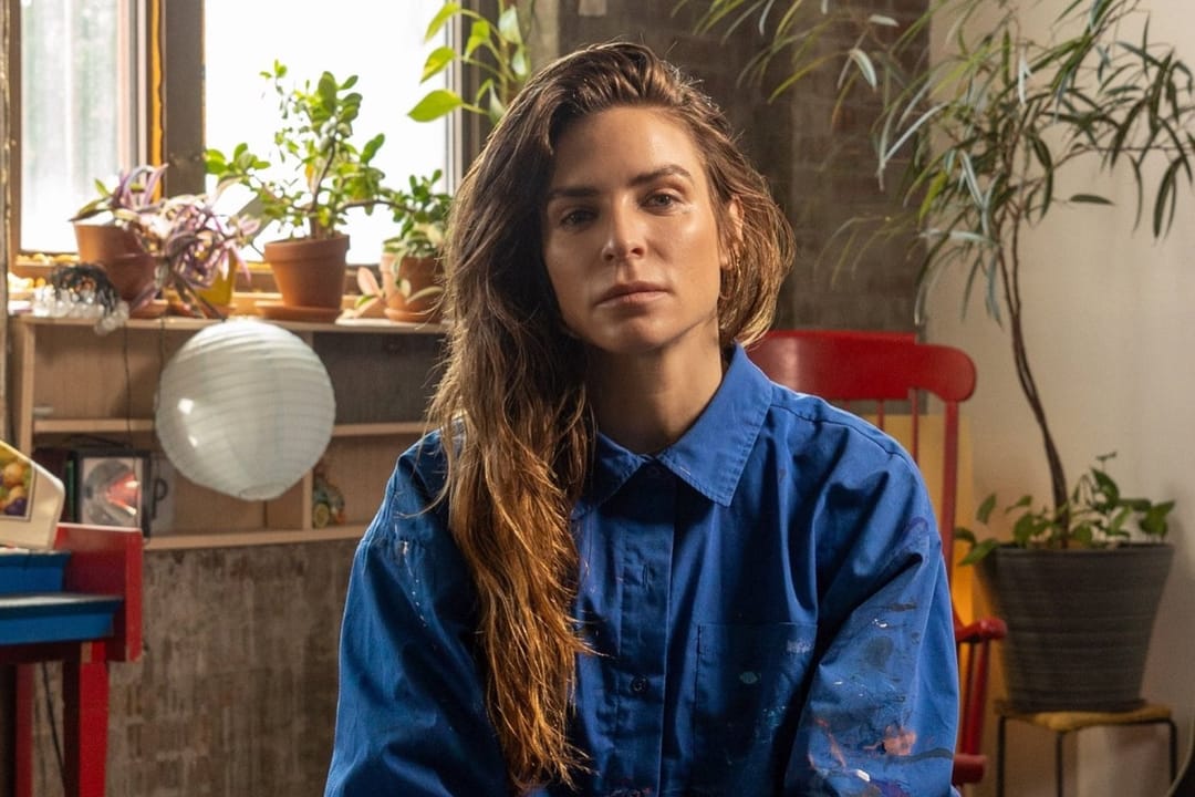 Annina Roescheisen con una camisa azul manchada de pintura en su estudio, con plantas en la ventana detrás