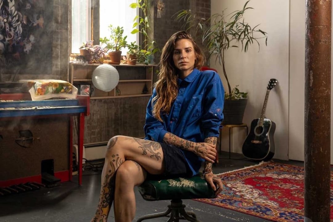 Annina Roescheisen seated in her studio, a guitar and plants behind her