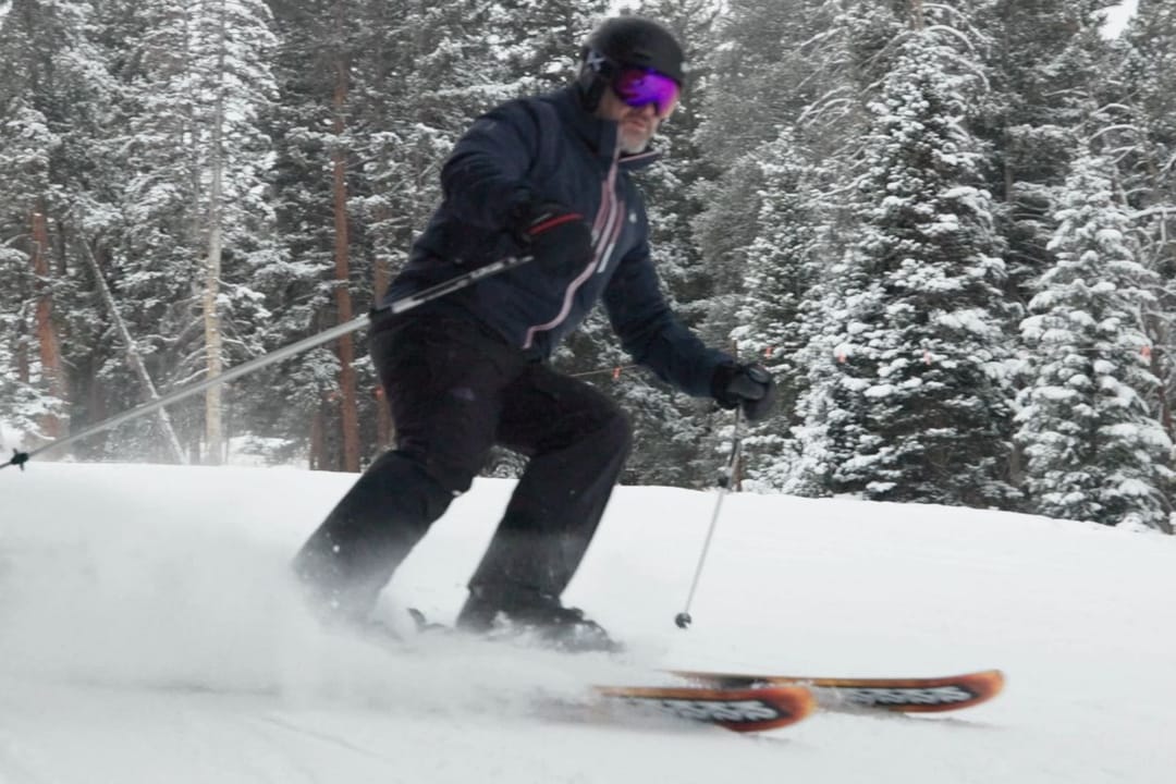 Skier carving through fresh snow among snowy pines at Beaver Creek