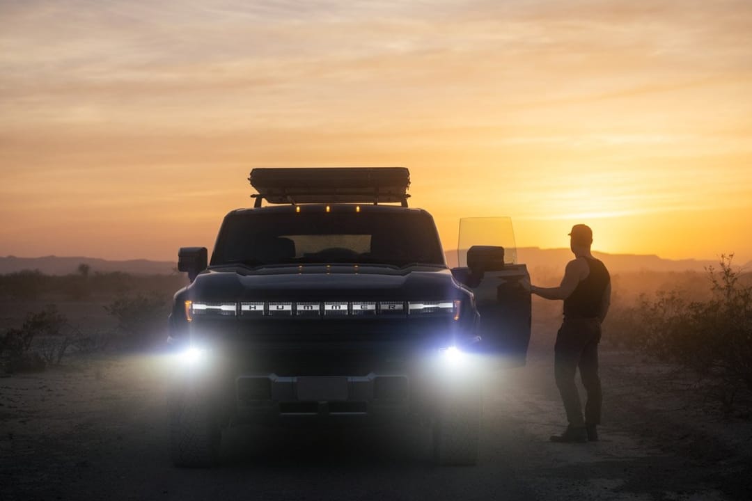 GMC Hummer EV con las luces encendidas al atardecer y un hombre junto a la puerta abierta