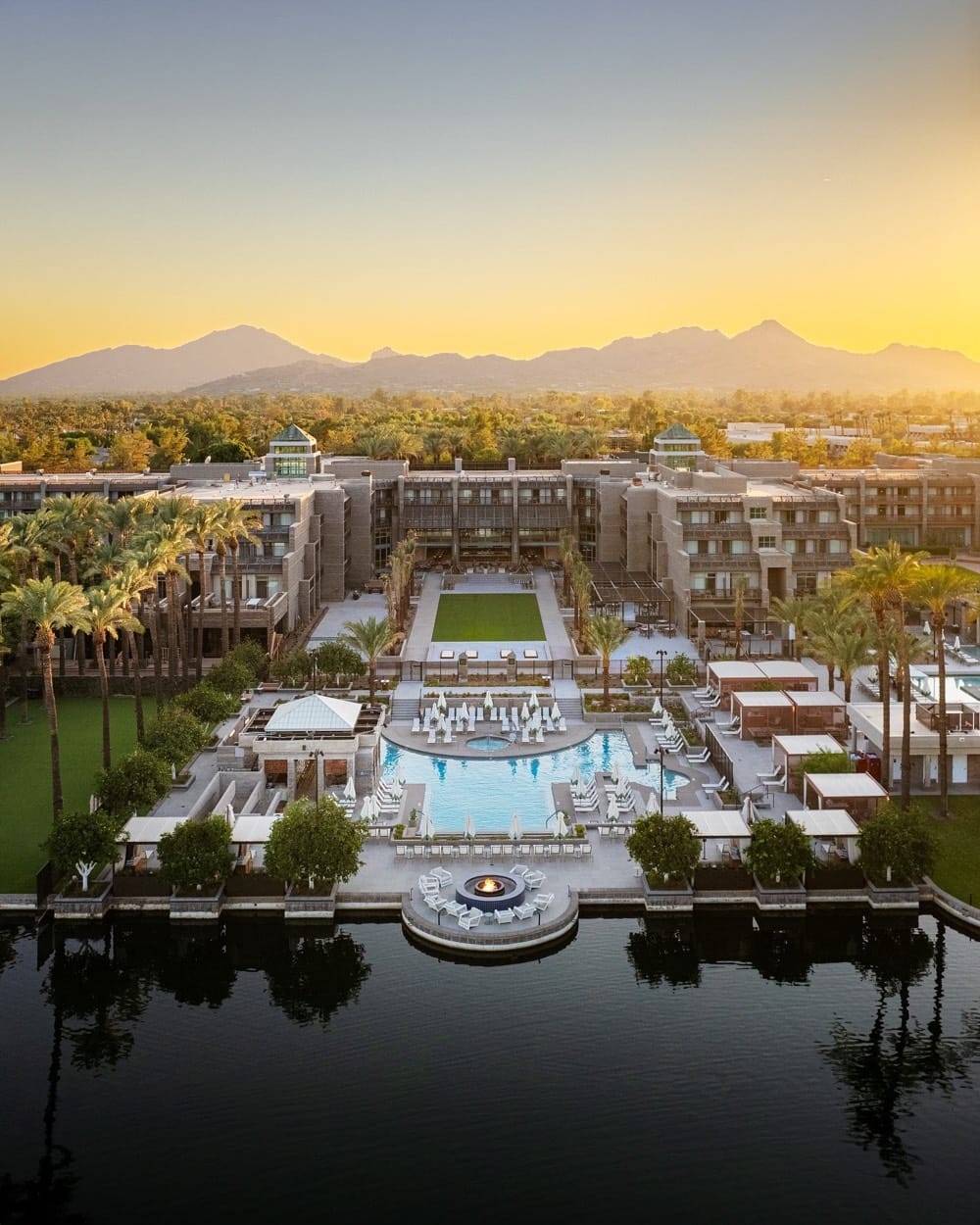 Grand Hyatt Scottsdale desde el aire al atardecer, con las piscinas y el lago al frente y montañas detrás