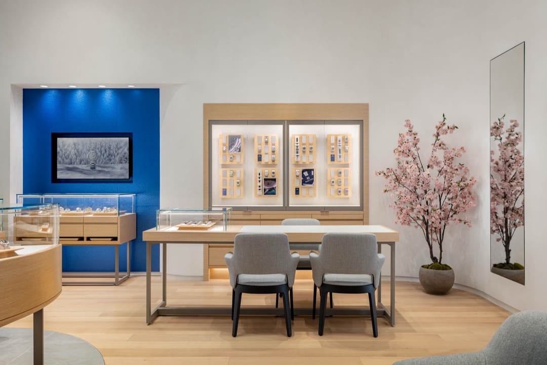Grand Seiko desk between a blue wall and a blossom branch, watch displays behind