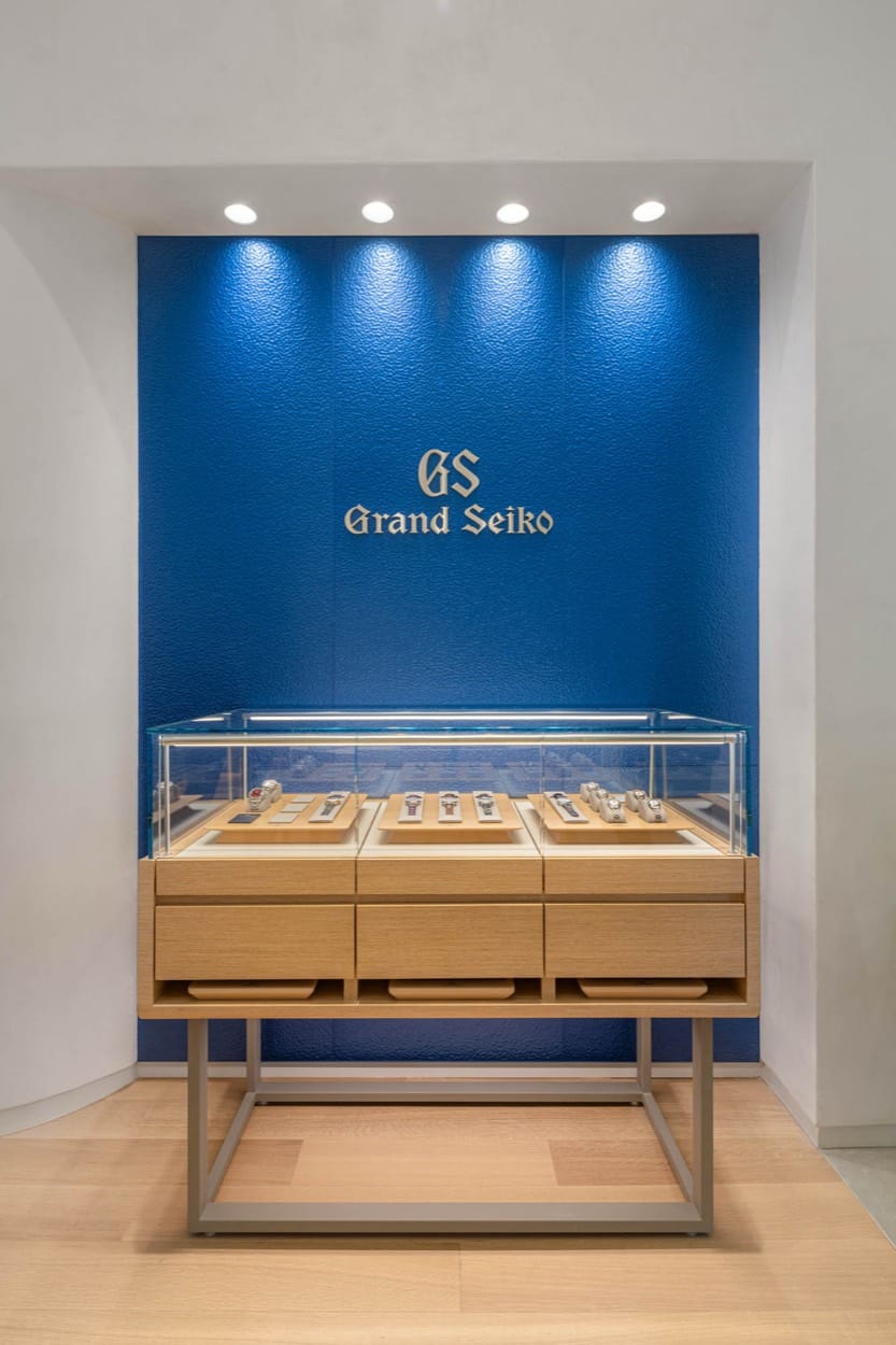 Grand Seiko logo on a lit blue wall above a watch display