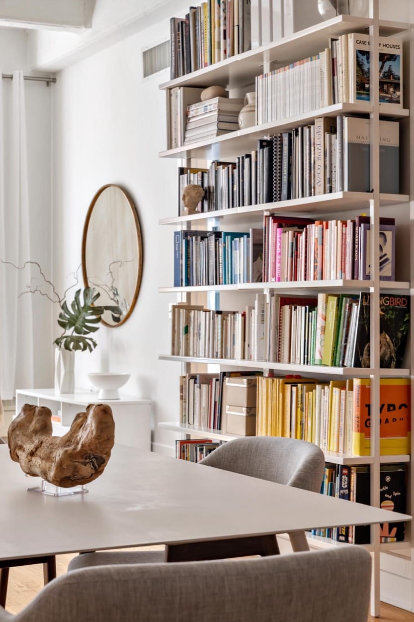 Mesa de comedor junto a libreros de piso a techo, un espejo redondo y una escultura de madera