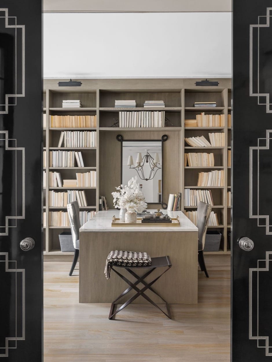 Biblioteca de casa vista a través de puertas negras abiertas, con escritorio y banco frente a libreros llenos