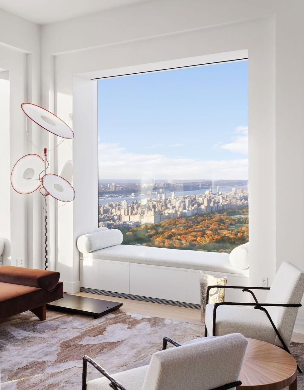 Sala con banco junto a la ventana que enmarca Central Park en otoño y el skyline de la ciudad