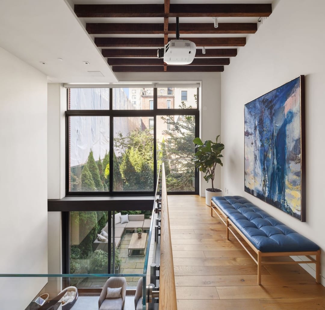 Loft con mezzanine, vigas de madera oscura, una banca azul y una gran pintura abstracta