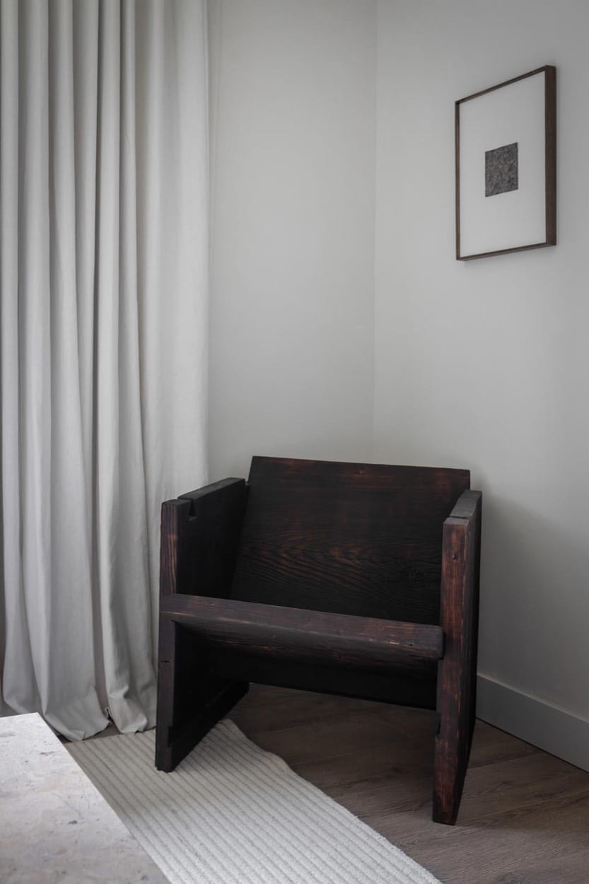 Dark wood chair in a quiet corner by linen curtains, a framed print above