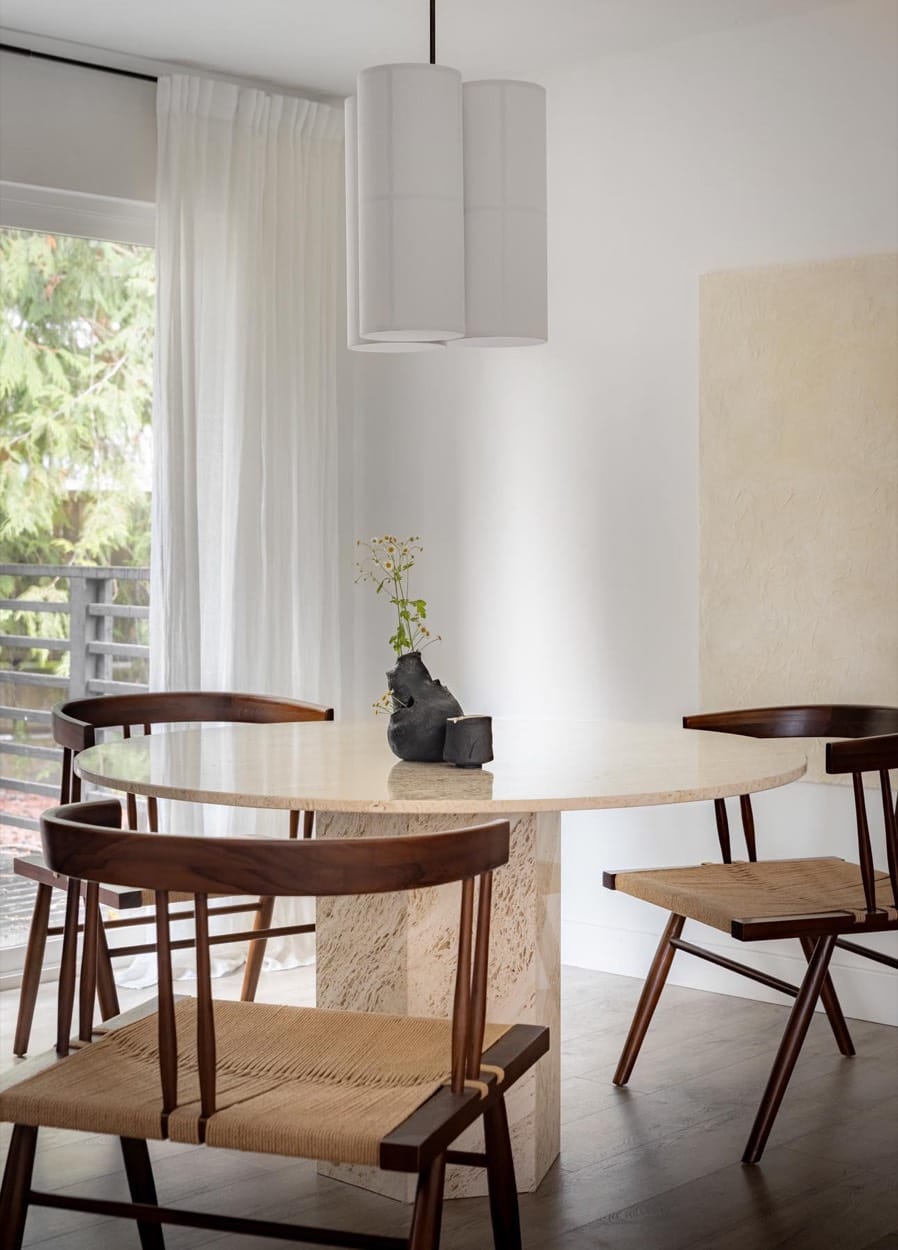 Comedor con mesa de pedestal de piedra, sillas de madera y fibra, y una lámpara de papel