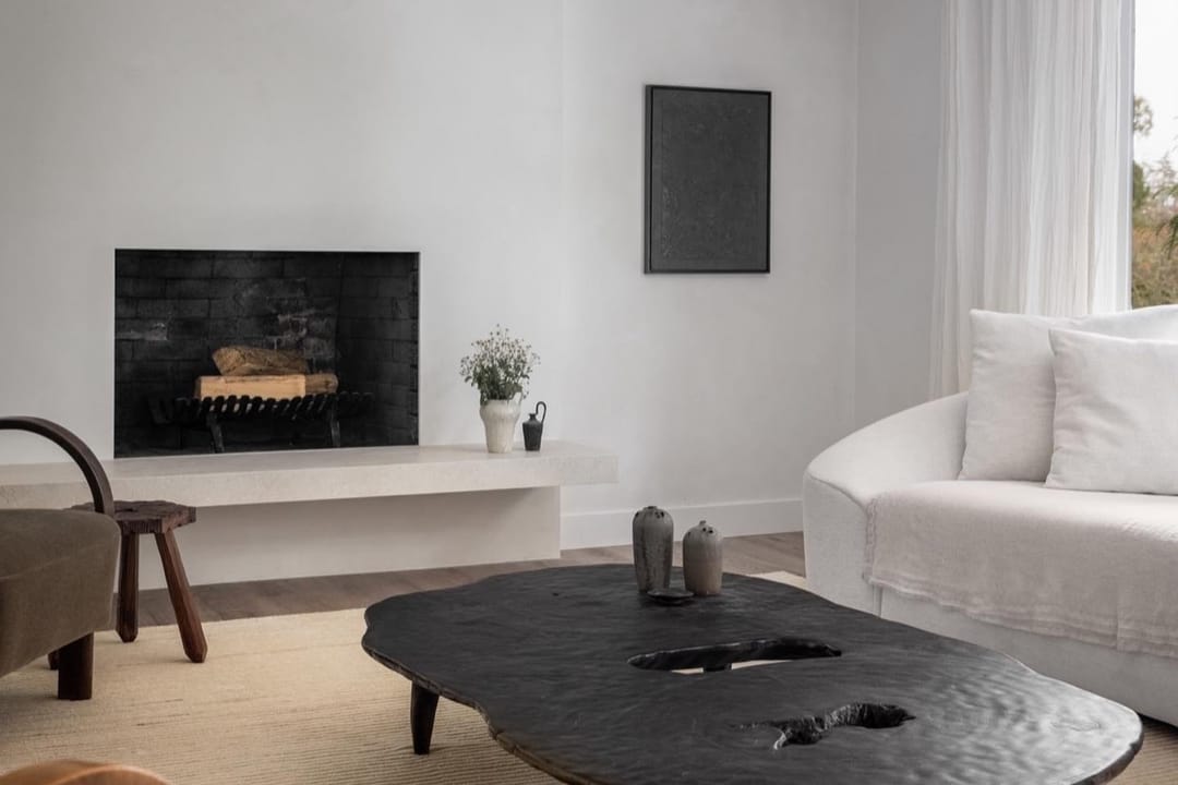 Sala minimalista con mesa de centro negra esculpida, sofá blanco curvo y chimenea