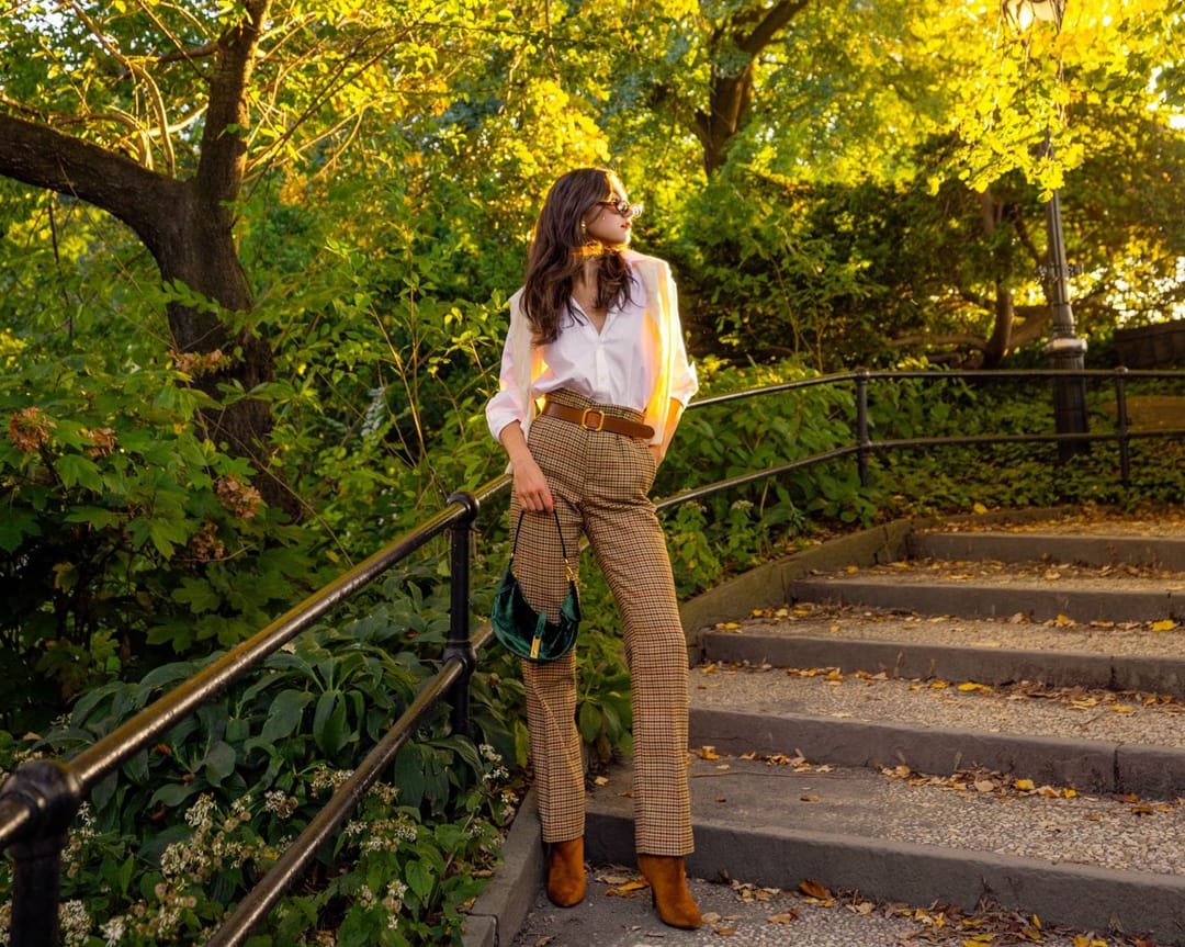 Woman in a white blouse and tan trousers on park steps under golden trees