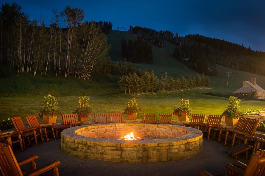 Fogata de piedra rodeada de sillas de madera al anochecer, bajo las pistas, Park Hyatt Beaver Creek