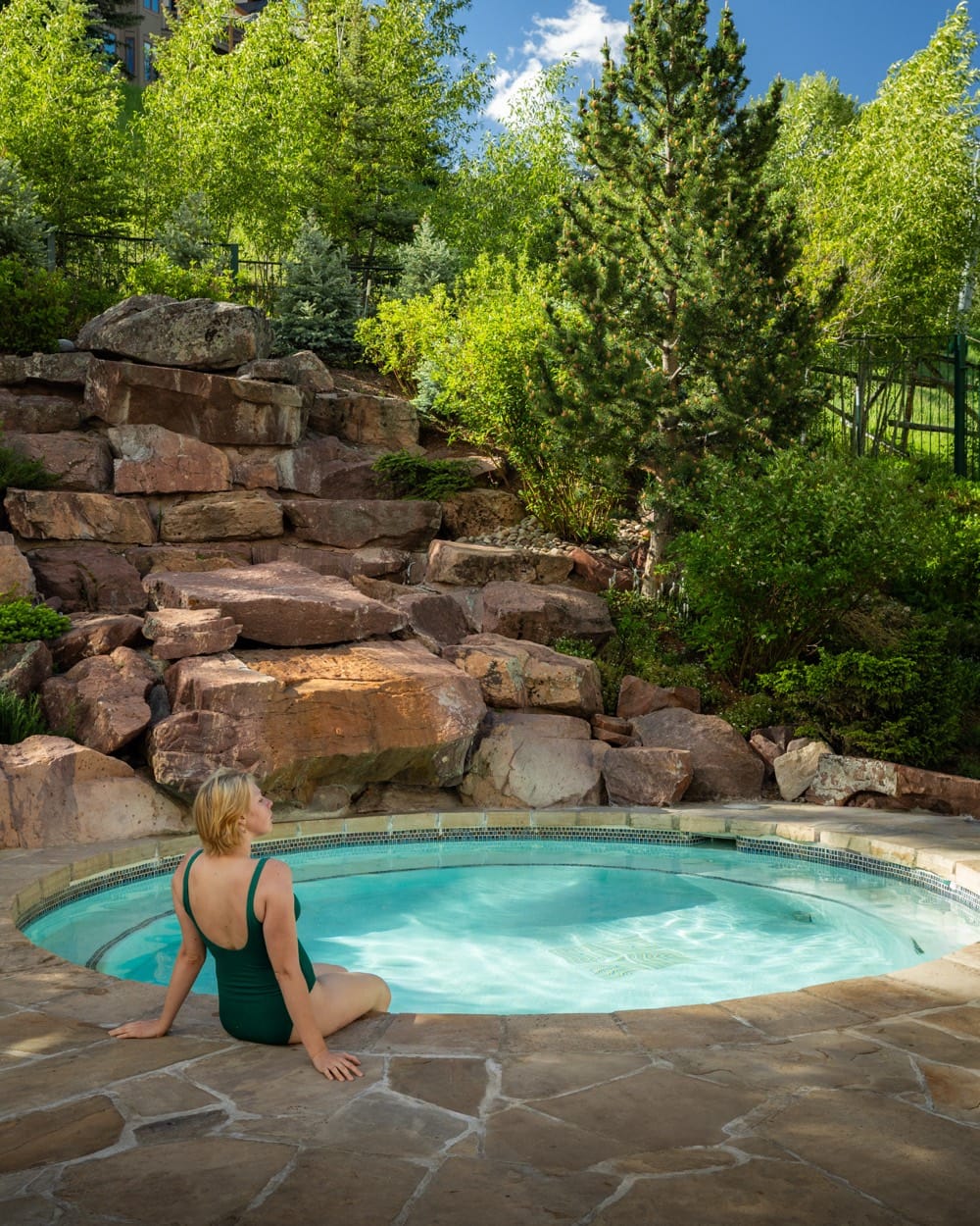 Mujer en traje de baño verde al borde de un jacuzzi entre rocas y álamos, Park Hyatt Beaver Creek