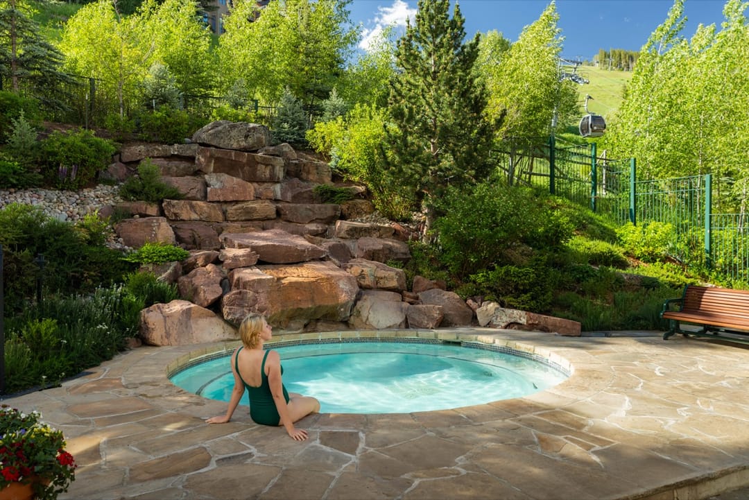 Woman at the edge of a hot tub below a rock waterfall in summer, Park Hyatt Beaver Creek