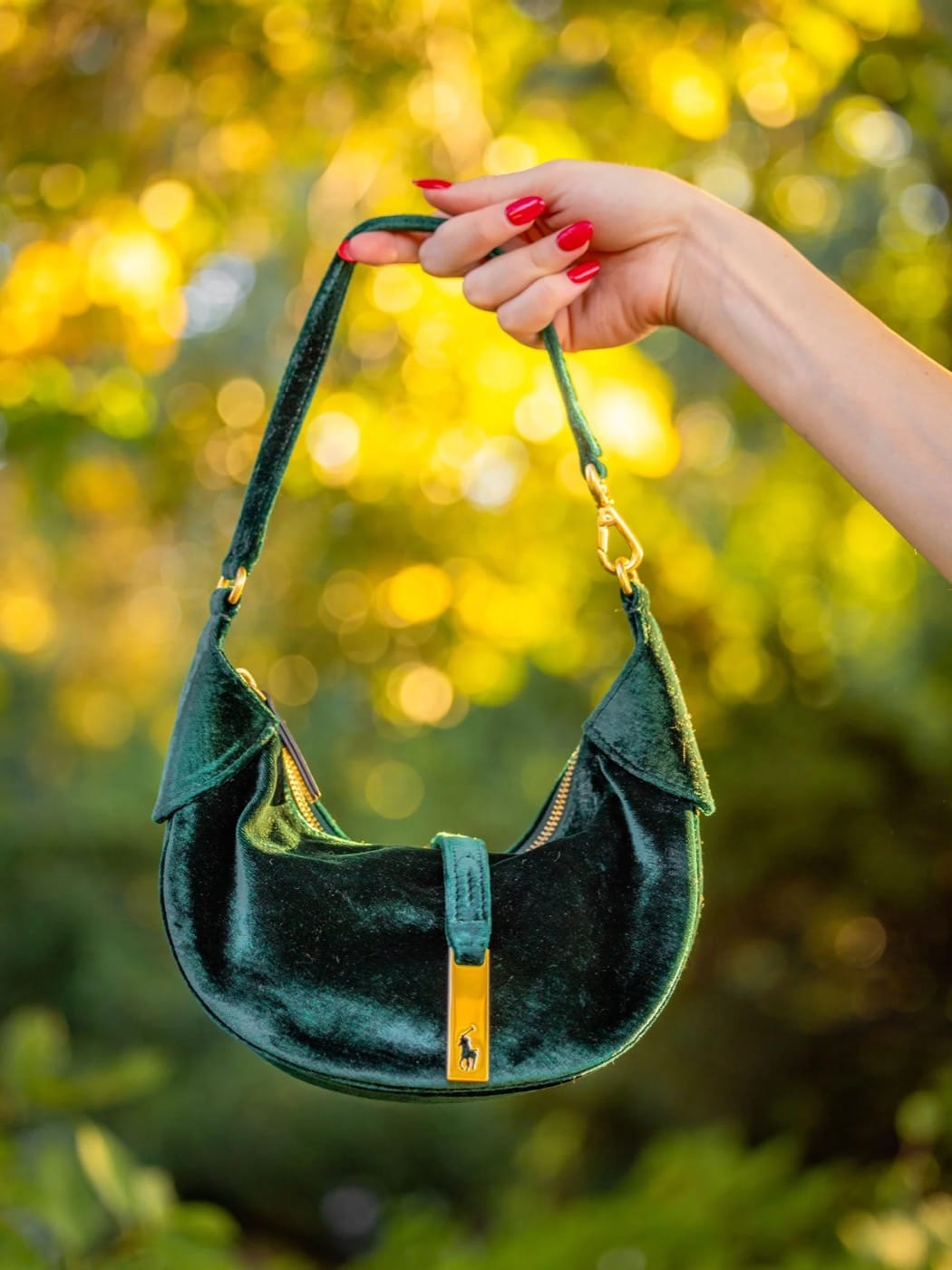 Bolso de terciopelo verde de Polo Ralph Lauren sostenido frente a hojas doradas de otoño