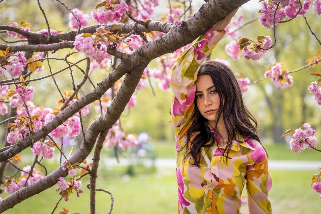 Portrait of a woman in a floral blouse under a pink cherry blossom branch