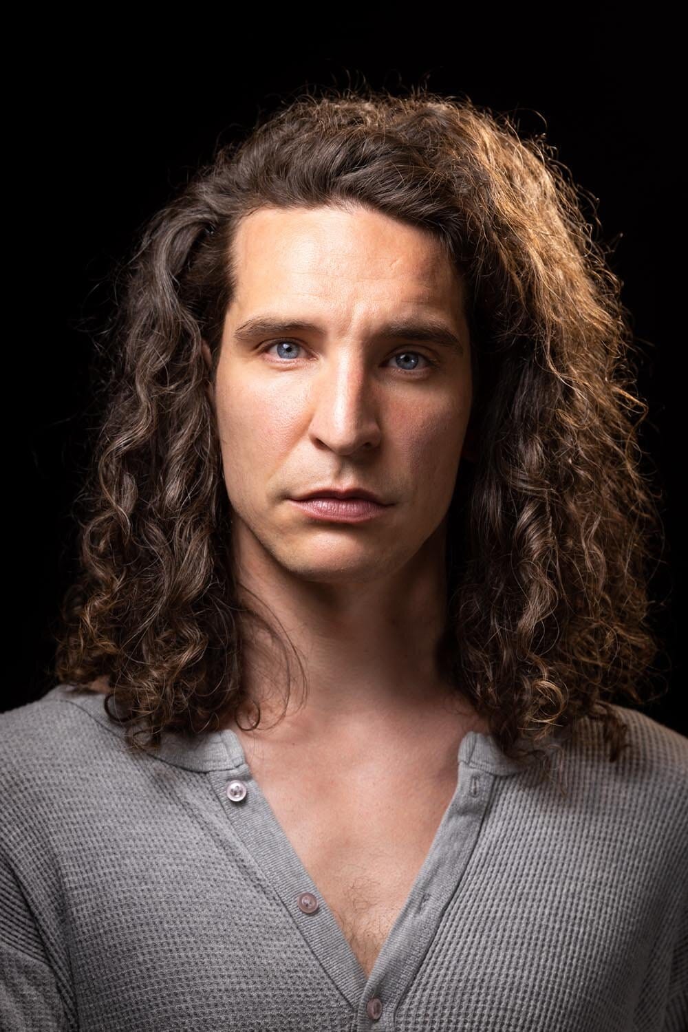 Studio portrait of a man with long curly hair against black