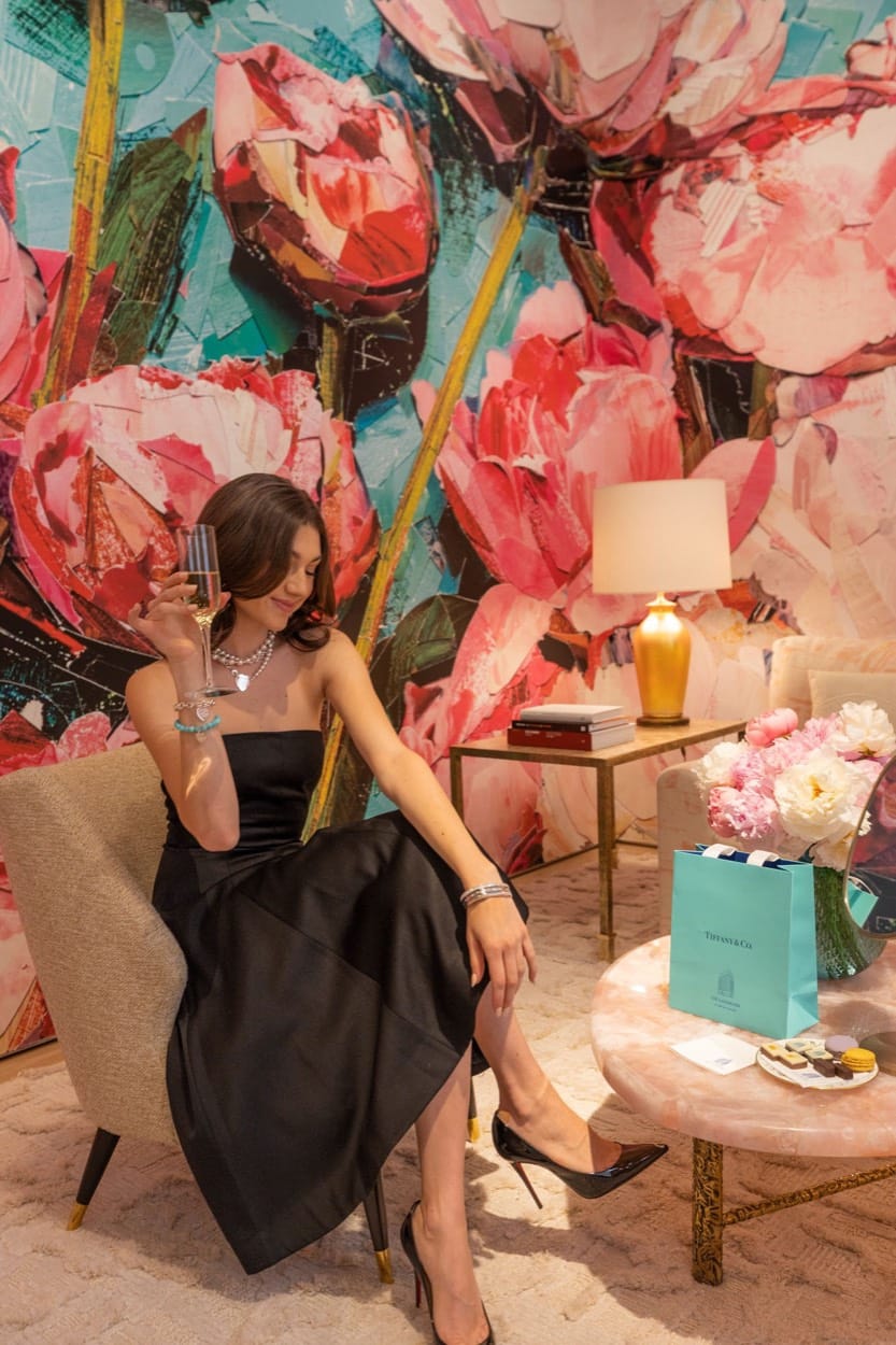 Kate Bartlett con champaña en una sala de peonías pintadas, con una bolsa de Tiffany & Co. a su lado